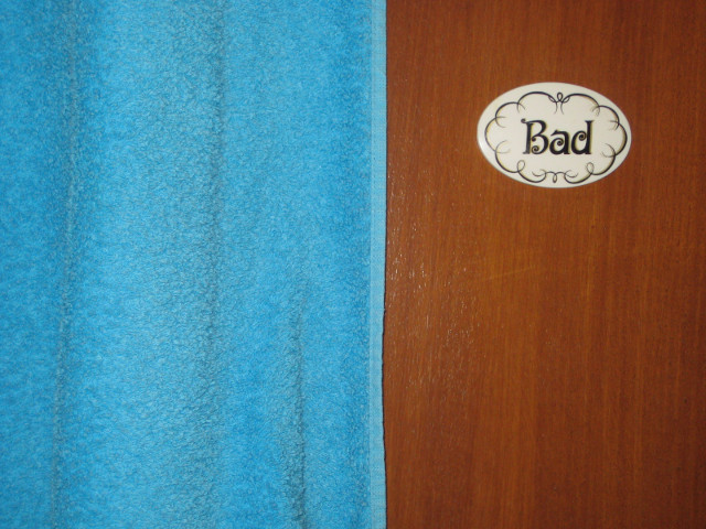 A german-friendly bathroom door draped with towel, sign says 'Bad'