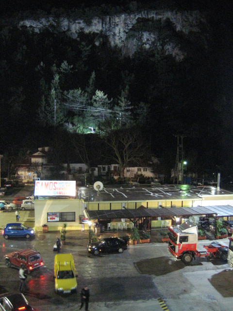 Karlóvassi harbor, 4:00am floodlit cliffs behind a few vehicles boarding the ferry, which is out of sight under the photographer