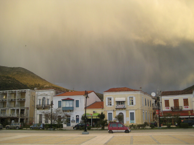 Vathí - Early morning rain Rain behind two-storey, tile-roofed buildings.