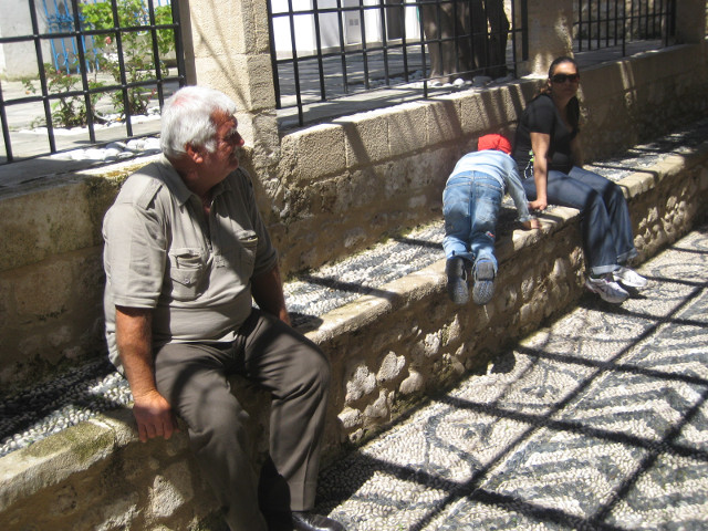 Caretaker at the Synagogue white-haired man sitting on a low wall with some visitors