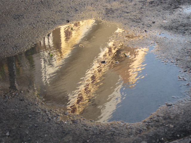 Reflection sunlit two-storys reflected in street puddle