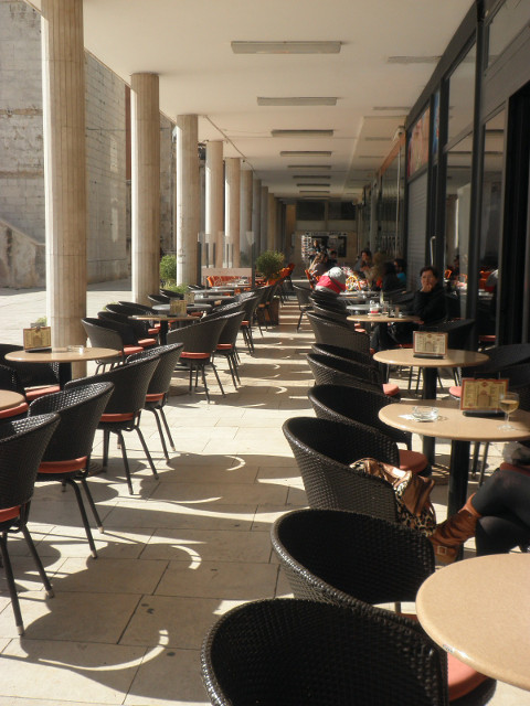 cafes on a major square chairs and tables under columned walkay