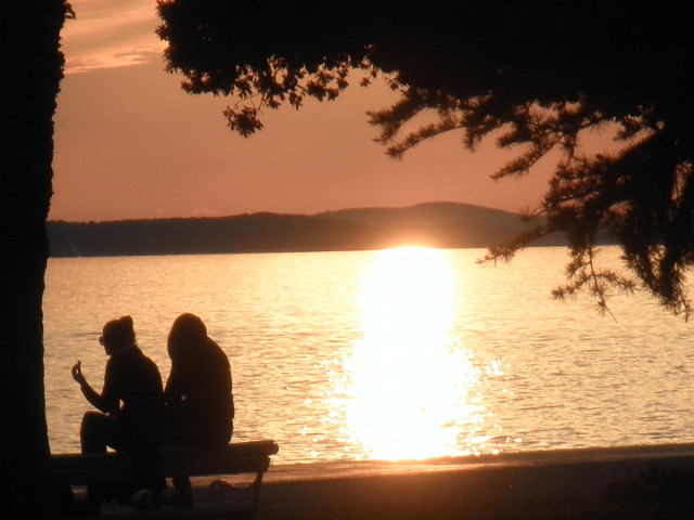 sunset couple seated, sun setting over sea and island