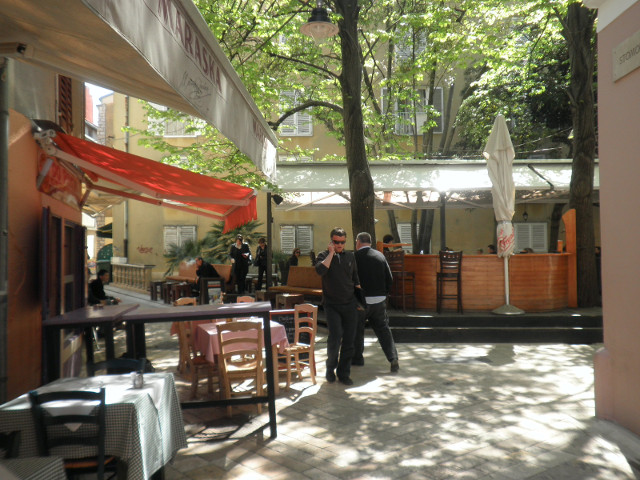 colorful cafe neighborhood narroow strees next to shaded plaza, all with cafe tables
