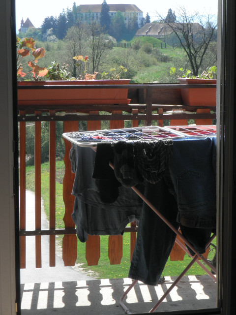 Castle with laundry view through doorway, past drying laundry and potted plants, to dastle on hilltop